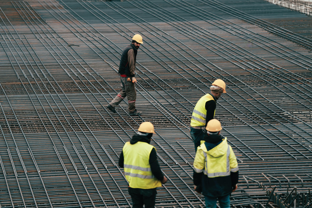 A collection of people in high-visibility protective gear and hardhats at a job site with rebar placed.