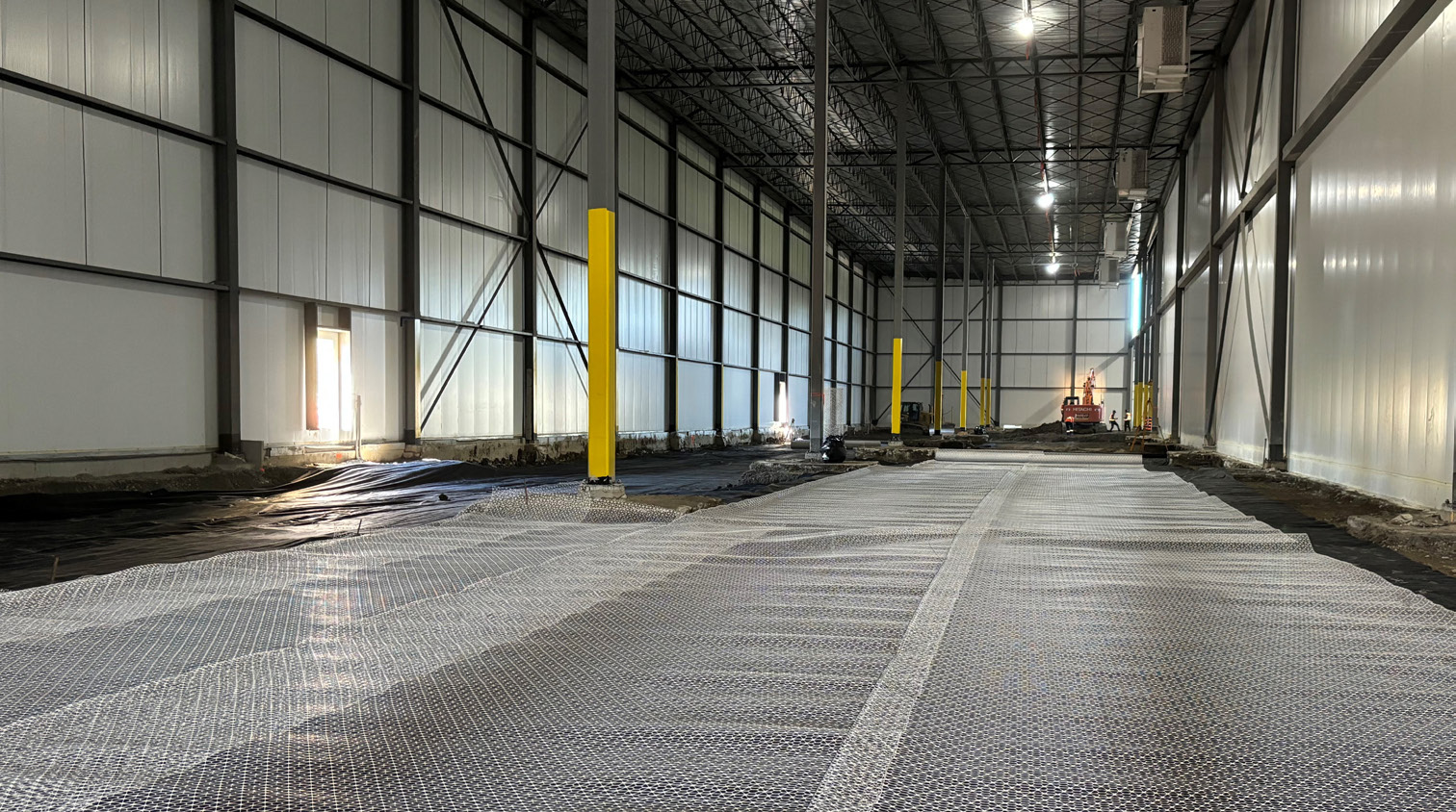 Warehouse interior with overlapping lines of geogrid placed down on the ground.