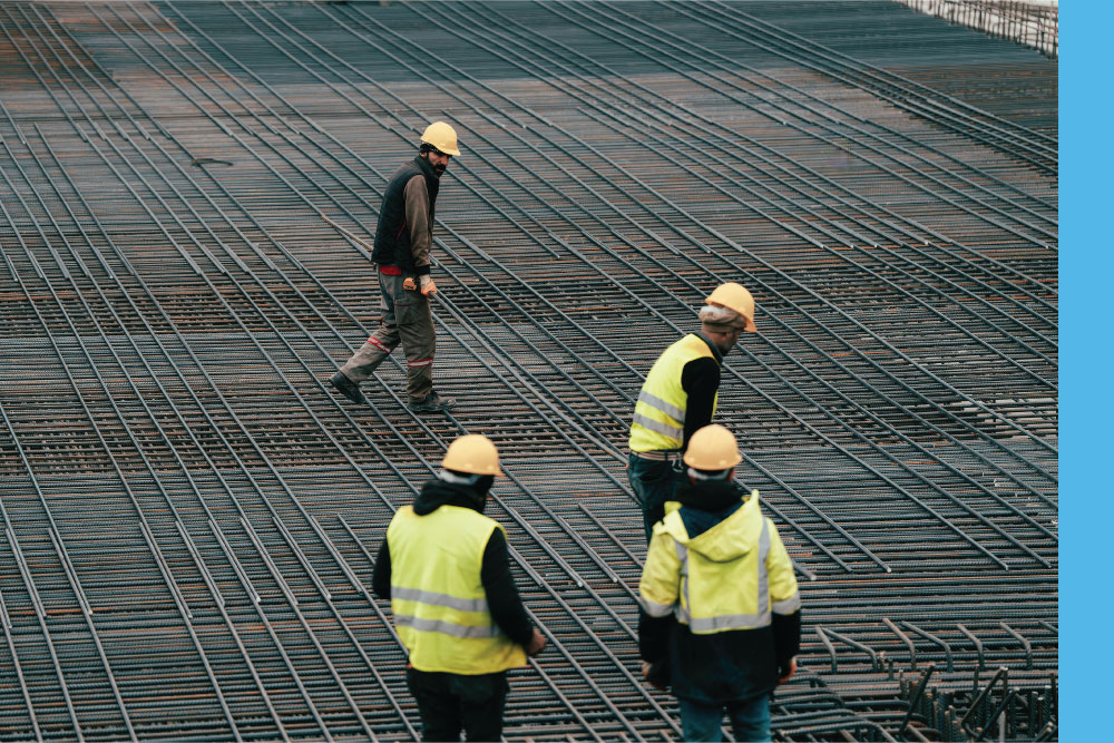 A collection of people in high-visibility protective gear and hardhats at a job site with rebar placed.