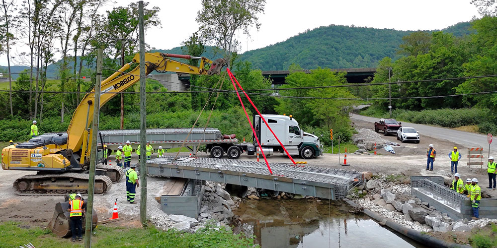 Construction equipment and works moving a new bridge deck into place.