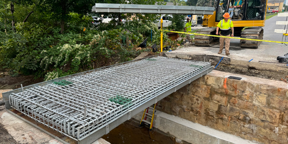Construction employees working with equipment to lower a bridge deck into place.